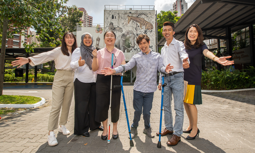 Group shot of six smiling individuals, consisting of persons with disabilities and those without.