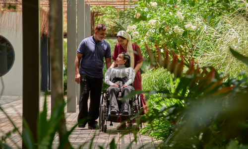 Man and woman pushing a wheelchair-user on a walk.