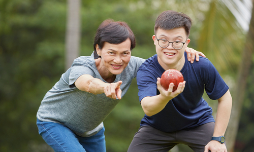 Mother smiling and instructing her son with disability how to play a sport.