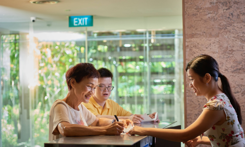 Woman helps a caregiver fill up a form over the counter.