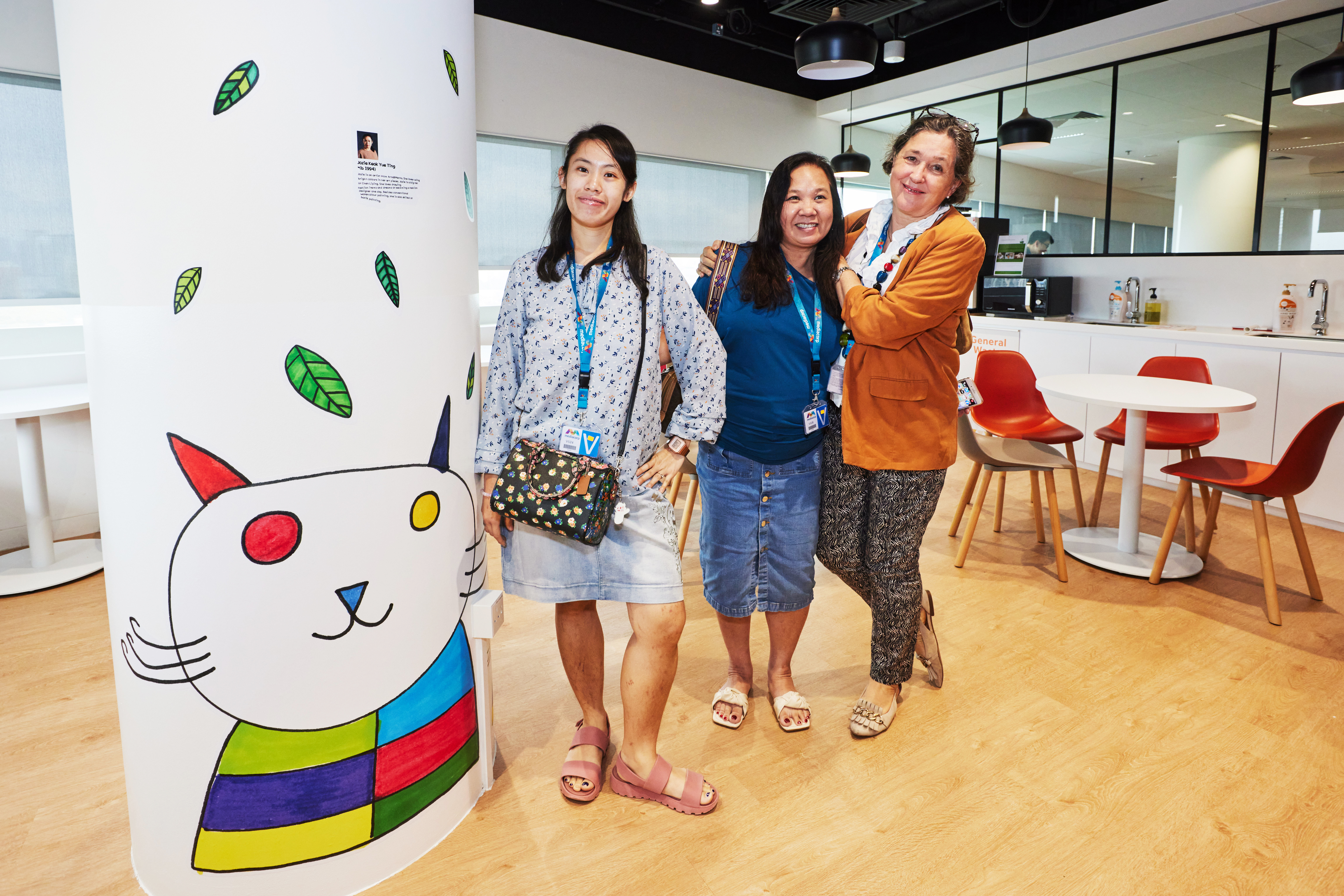 Jozie Keok - Artist with autism from Metta Welfare Association, poses with her mother and Dr Esther by her wall sticker mural depicting an artistic rendition of a cat