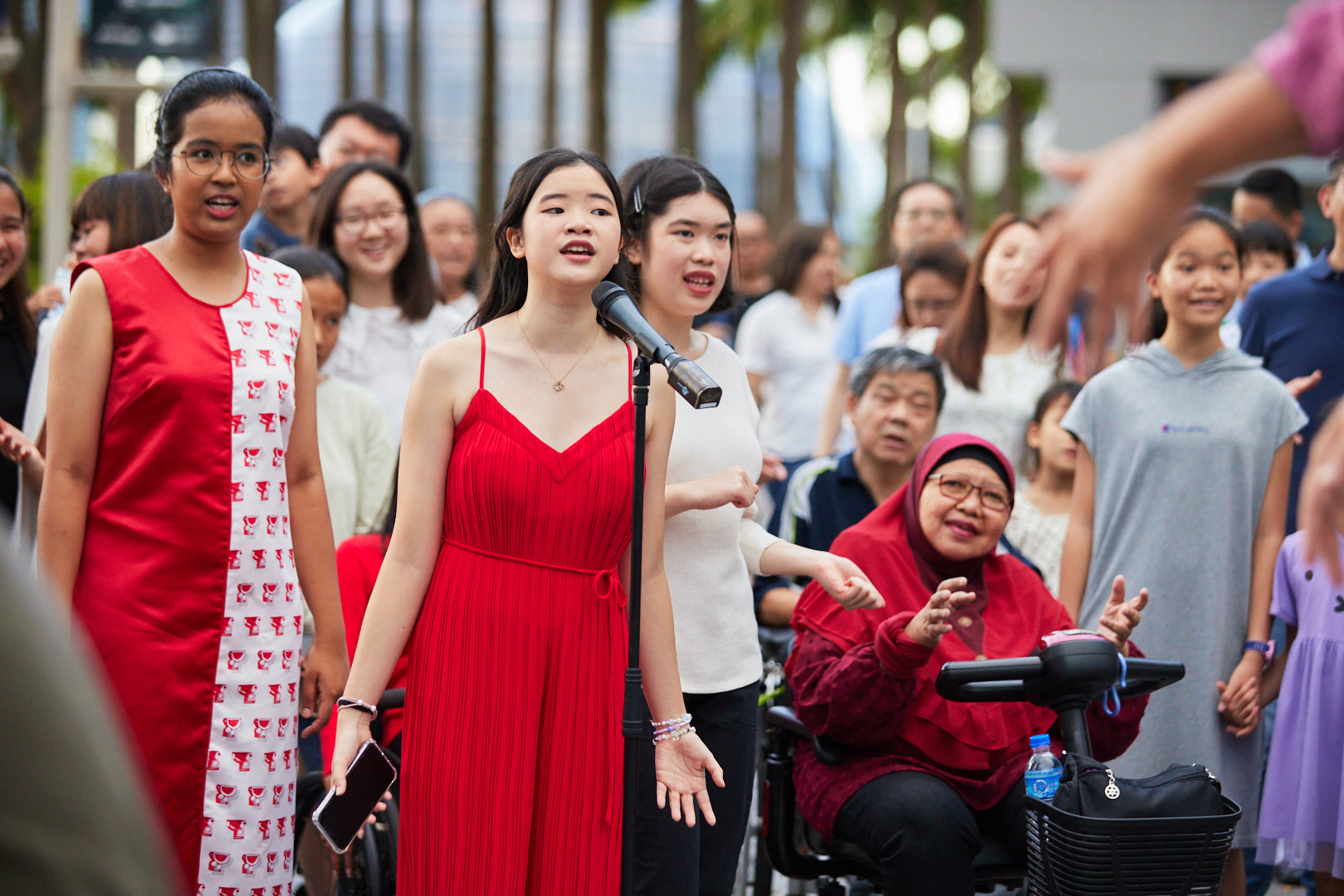 A girl in red sings in front of a mic, surrounded by fellow singers of the inclusive choir.