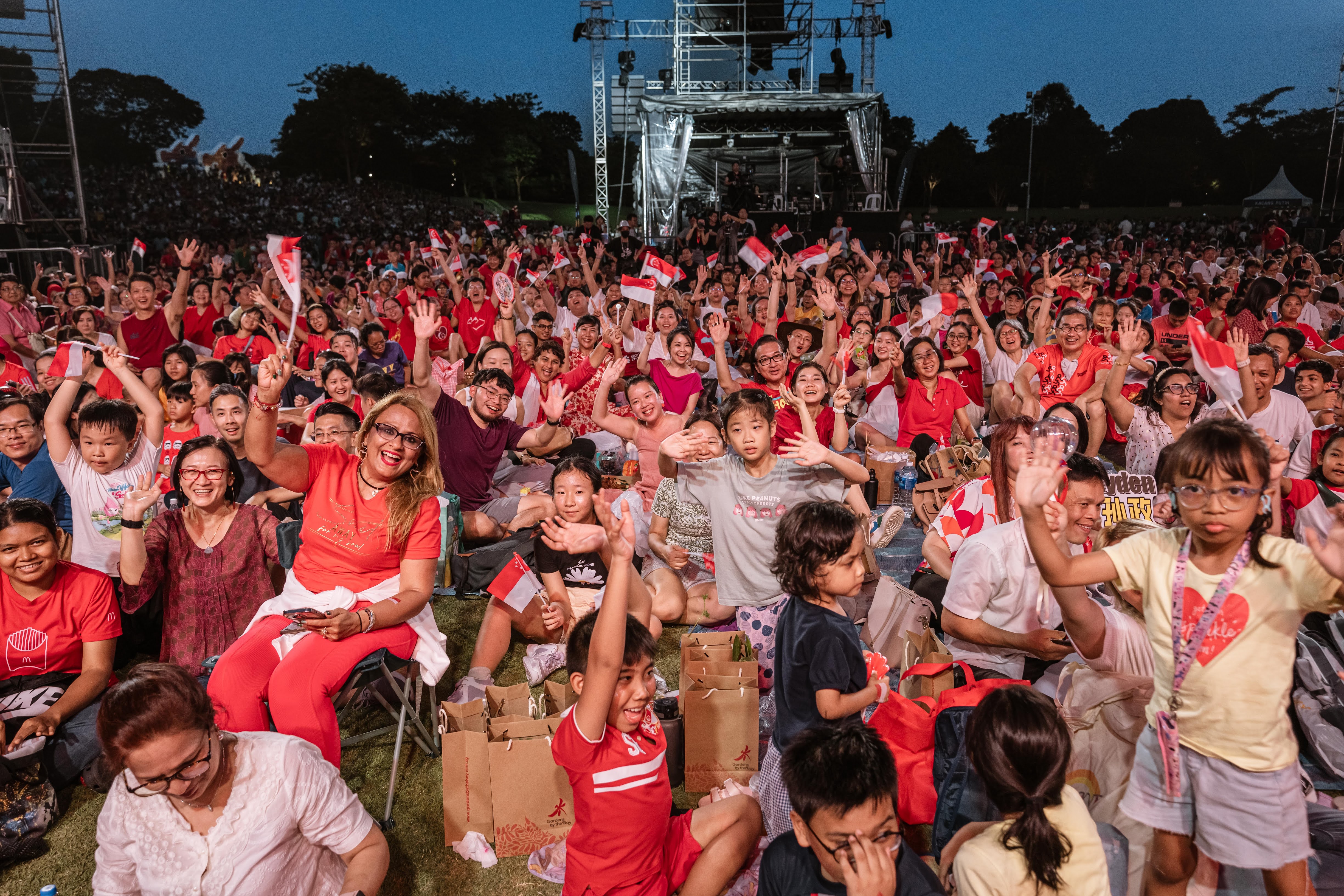 A crowd of people dressed in red waving their Singapore flags at the National Day Concert.