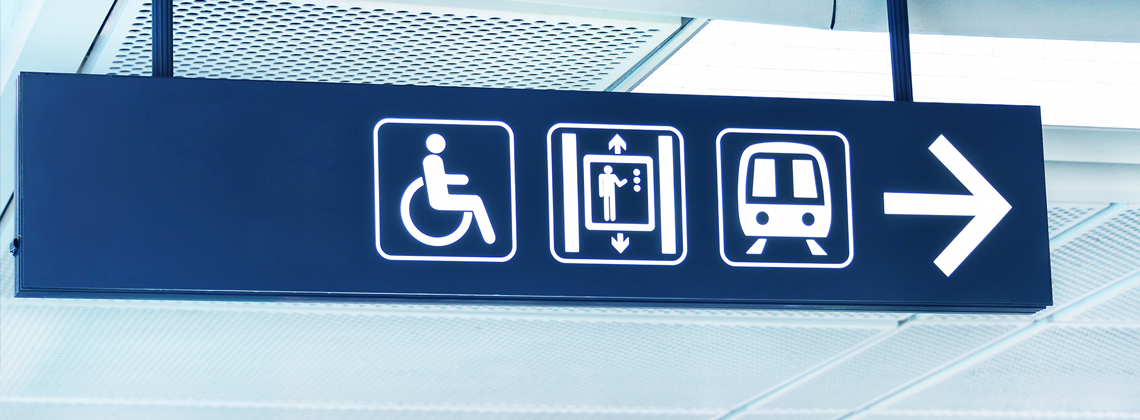 Photo of a directional sign showing an accessibility symbol, lift symbol, and a train symbol.