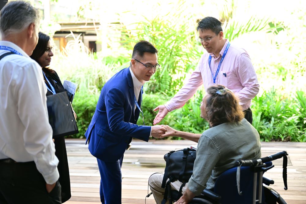 Photo of a man in a suit shaking hands with another man using a wheelchair.